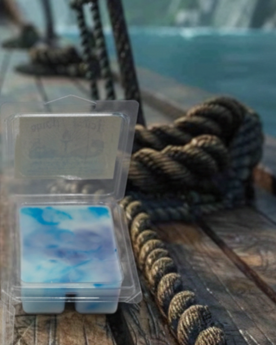 Packaged blue white and violet marbled wax melts on a wooden pirate ship deck surface with a rope and blurred ocean background
