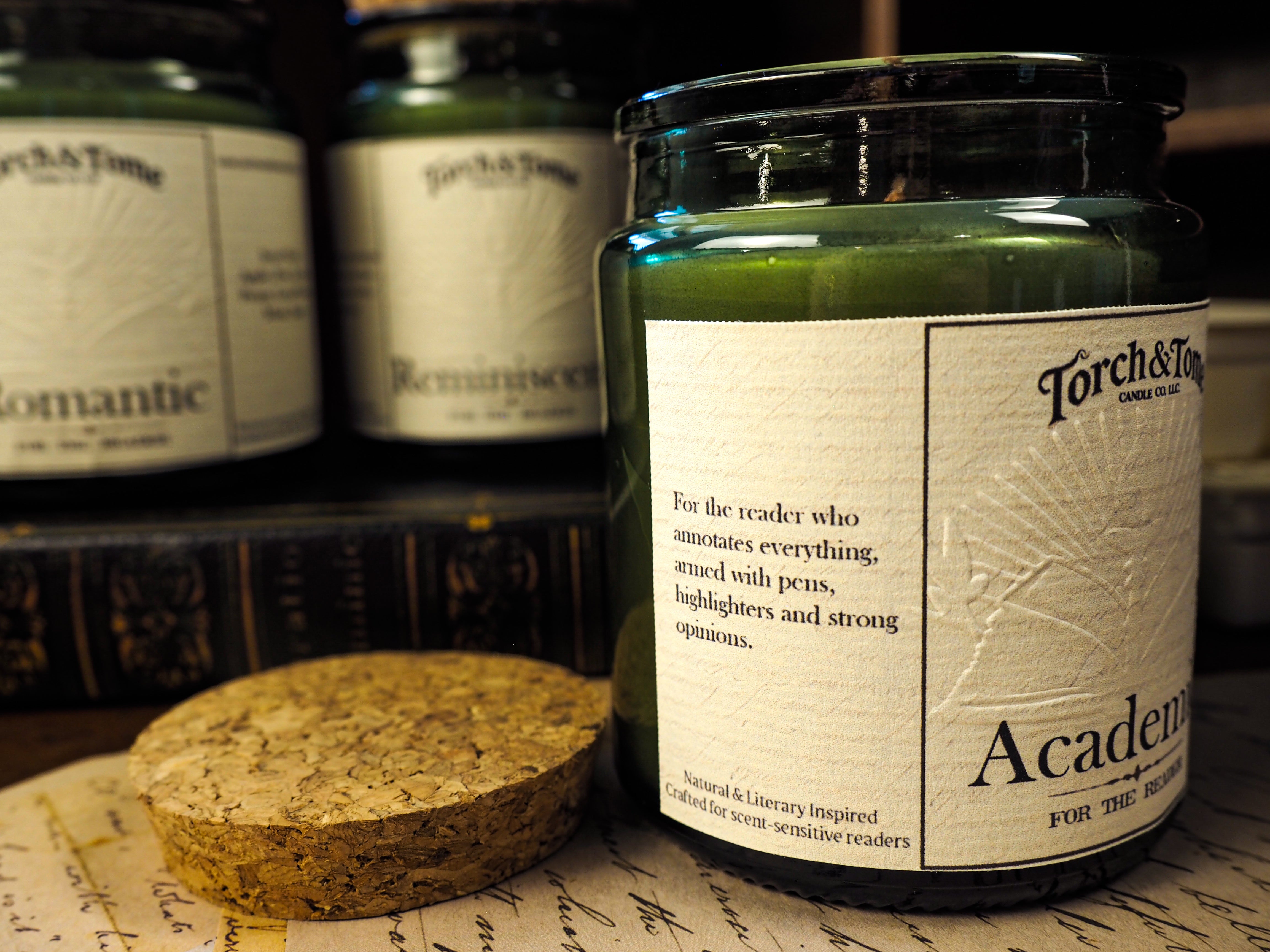 Jar of 'Academic' candle with a label, surrounded by other candles on a textured surface.