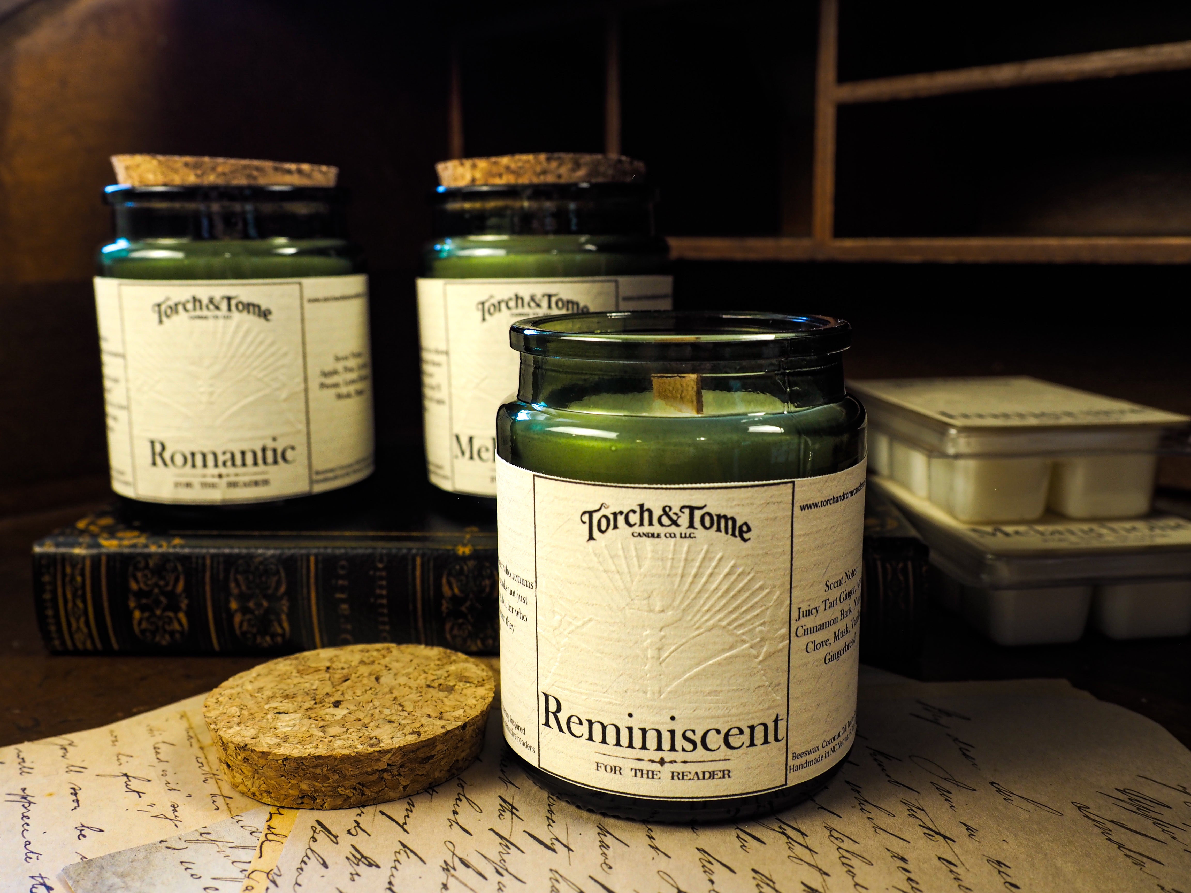 Three green glass candles sitting on a wooden desk, featuring cork lid and written notes on the tabletop