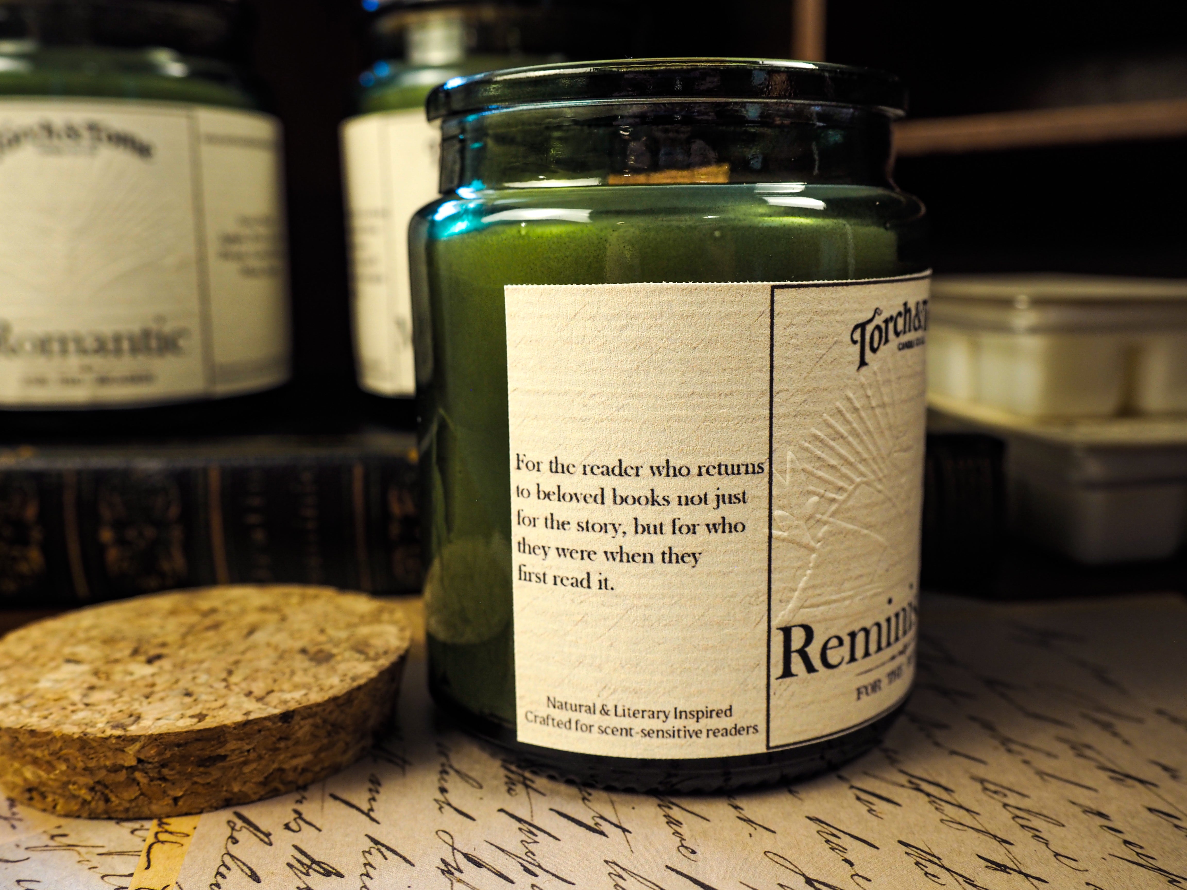 Candle jar labeled 'Reminiscence' on a surface with other similar jars in the background.