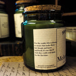 Green candle in a glass jar with a label on a surface with books and papers.