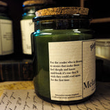 Green candle in a glass jar with a label on a surface with books and papers.