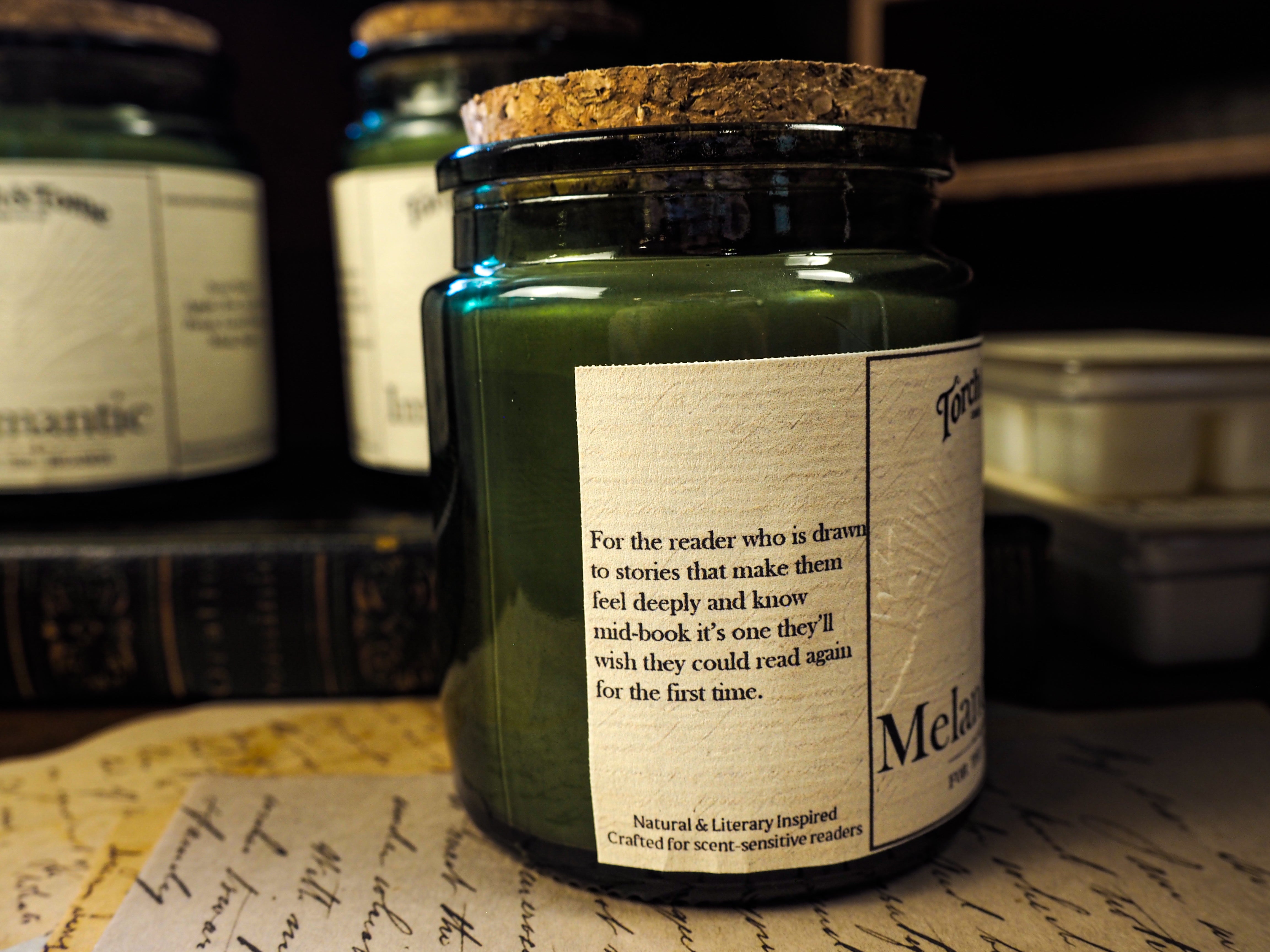 Green candle in a glass jar with a label on a surface with books and papers.