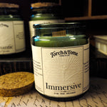 Torch & Tome candle labeled 'Immersive' on a surface with other candles in the background.