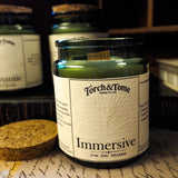 Torch & Tome candle labeled 'Immersive' on a surface with other candles in the background.