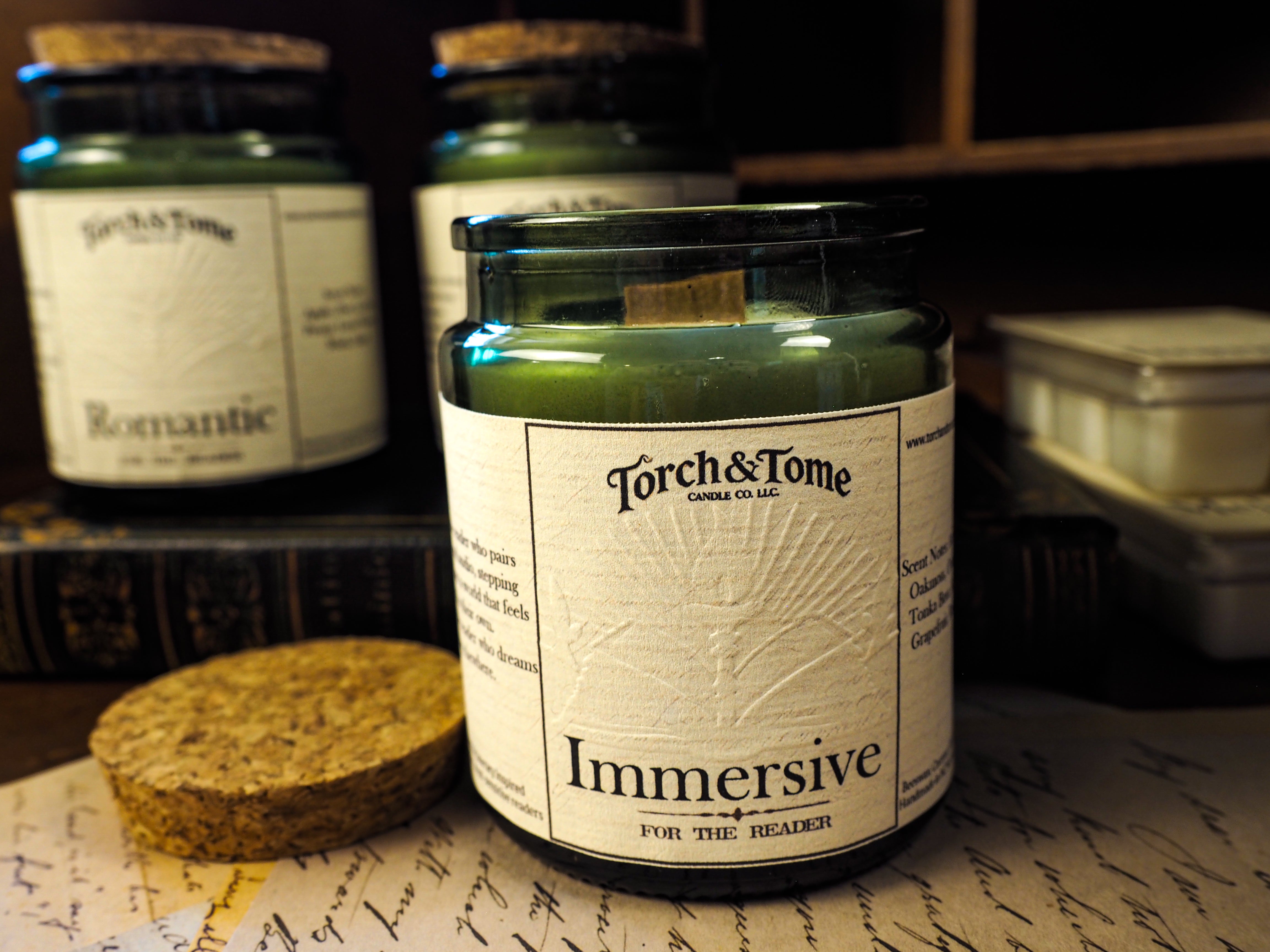 Torch & Tome candle labeled 'Immersive' on a surface with other candles in the background.
