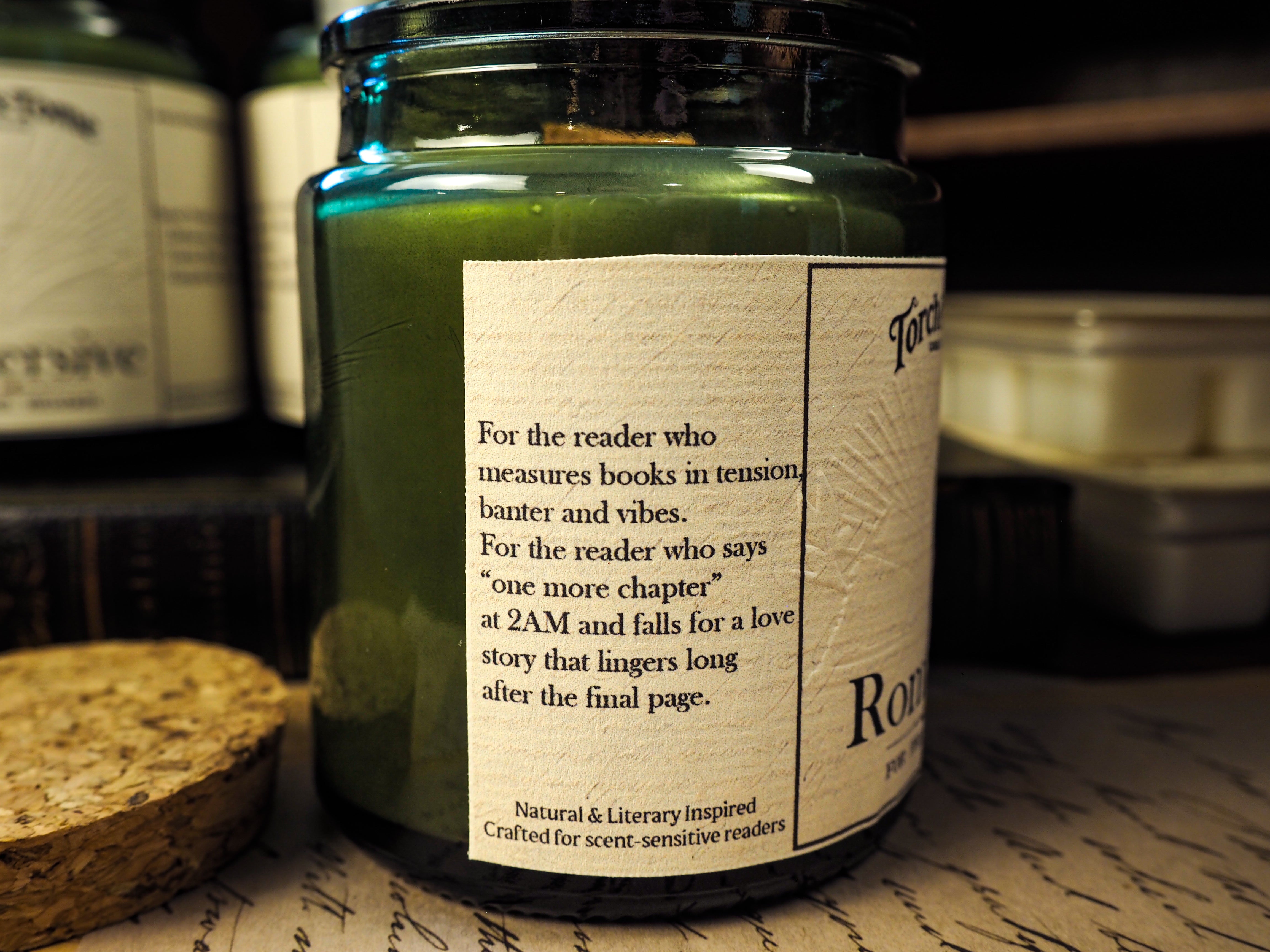 Candle jar featuring label with dedication to readers on the side sitting on top of a wood desk