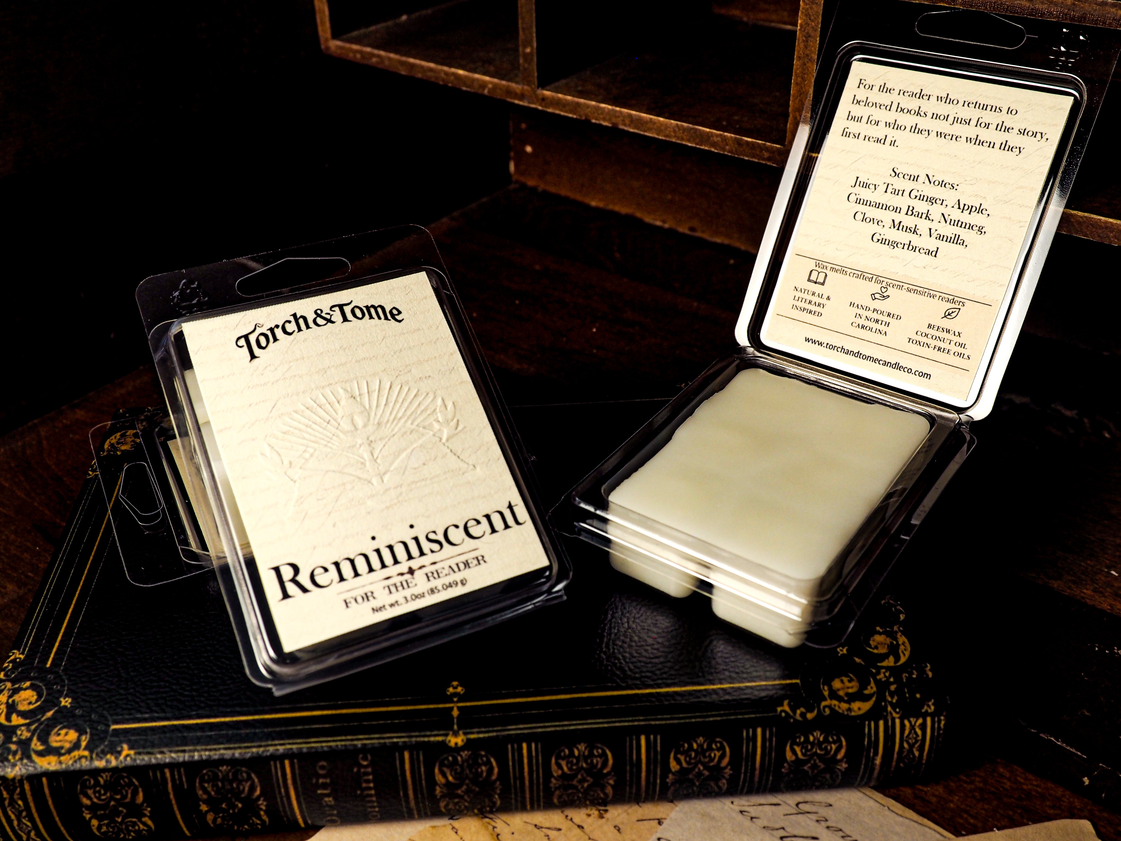 Two wax melt clamshell containters with 'Torch & Tome' branding on top of a book writing desk.