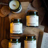 Collection of jars labeled 'Romantic', 'Melancholic', 'Immersive', and 'Academic' on a wooden surface with a candle and paper.