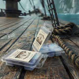 Torch & Tome wax melt clamshells featuring blue, white, and violet wax melts. Arranged on a wooden deck of a pirate ship next to bundled rope and ocean water and a scenic backdrop