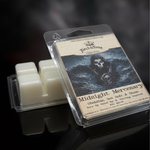 Midnight Mercenary packaged wax melts with a label featuring a skull design and two french swords on the label. Wax melt is propped against an upside down waxmelt clamshell showing the ivory beewax on a dark smoky background