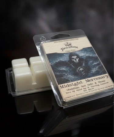 Midnight Mercenary packaged wax melts with a label featuring a skull design and two french swords on the label. Wax melt is propped against an upside down waxmelt clamshell showing the ivory beewax on a dark smoky background