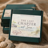 A dark green rectangular wax melt box with a large cream label reading 'THE LAST CHAPTER at Sea' is placed on a sandy surface with shells nearby. Three matching boxes are stacked behind it in a beach-like setting.