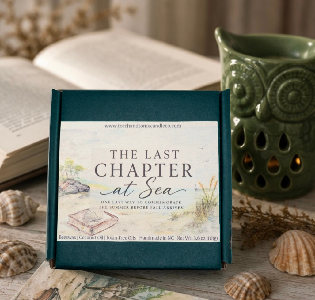 A square green gift box with a front label reading 'The Last Chapter at Sea' is displayed on a rustic tabletop with seashells, an open book, and a green owl-shaped candle holder in the background.