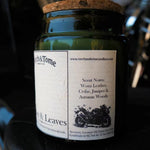 A dark green glass jar candle with a cork lid and a white paper label reading Torch & Tome, photographed close up against a dark, blurred background.