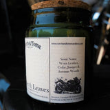 A dark green glass jar candle with a cork lid and a white paper label reading Torch & Tome, photographed close up against a dark, blurred background.